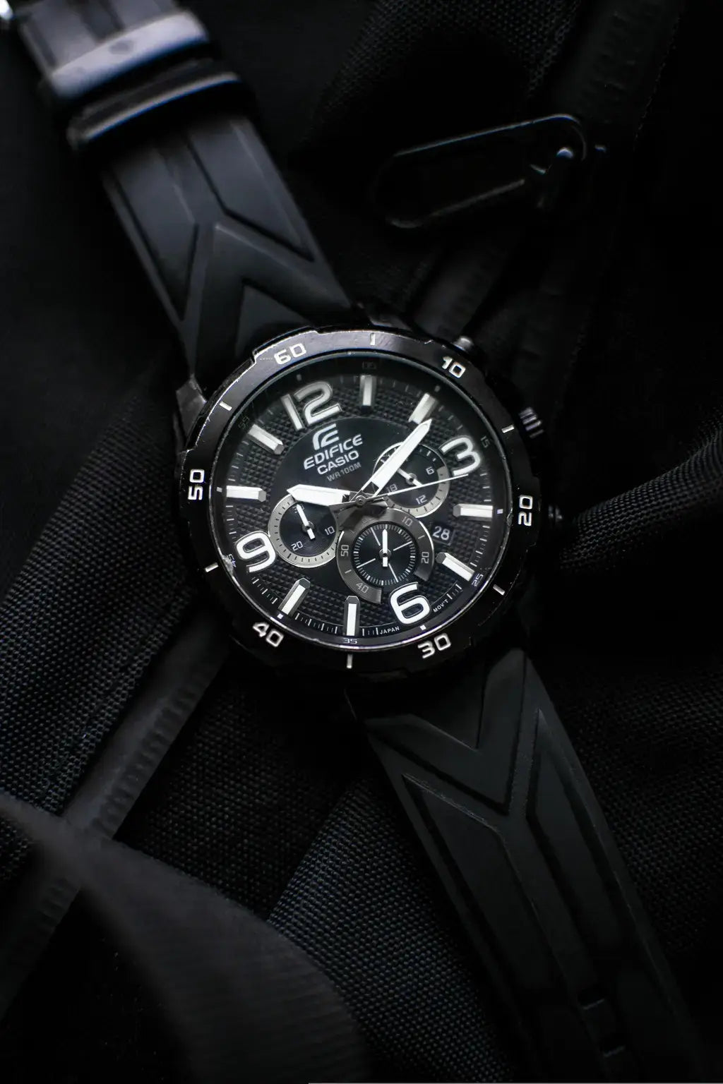 A black Casio Grandwave wristwatch with a matching black textured strap, resting on a black fabric background.